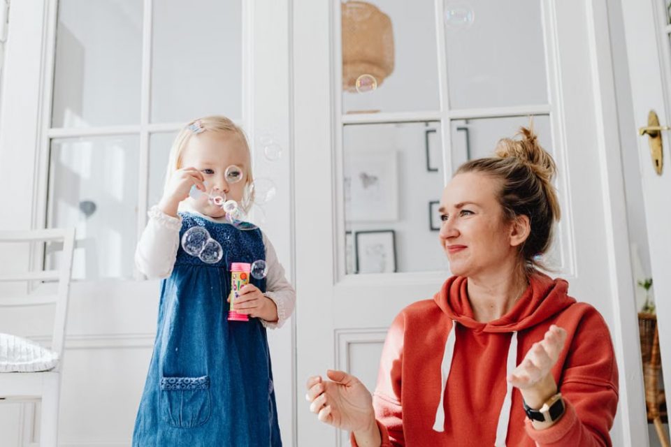 A joyful moment of a mother and daughter playing with bubbles indoors.